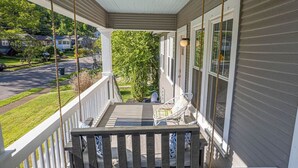 A covered porch with a wooden railing, a white chair, and a view of a residential street.