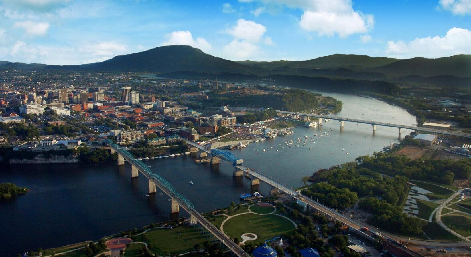An aerial view of a city with a river, bridges, and a mountainous backdrop.