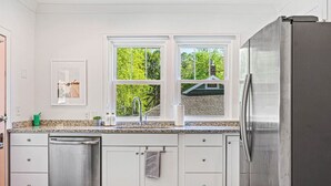 A kitchen with white cabinets, a stainless steel refrigerator, and a window with a view of greenery.