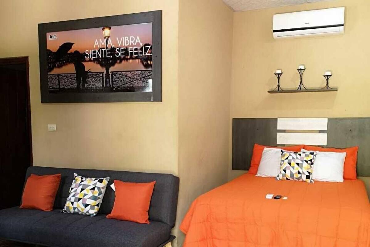A bedroom with a sofa, a bed, a wall-mounted air conditioner, and a decorative poster.