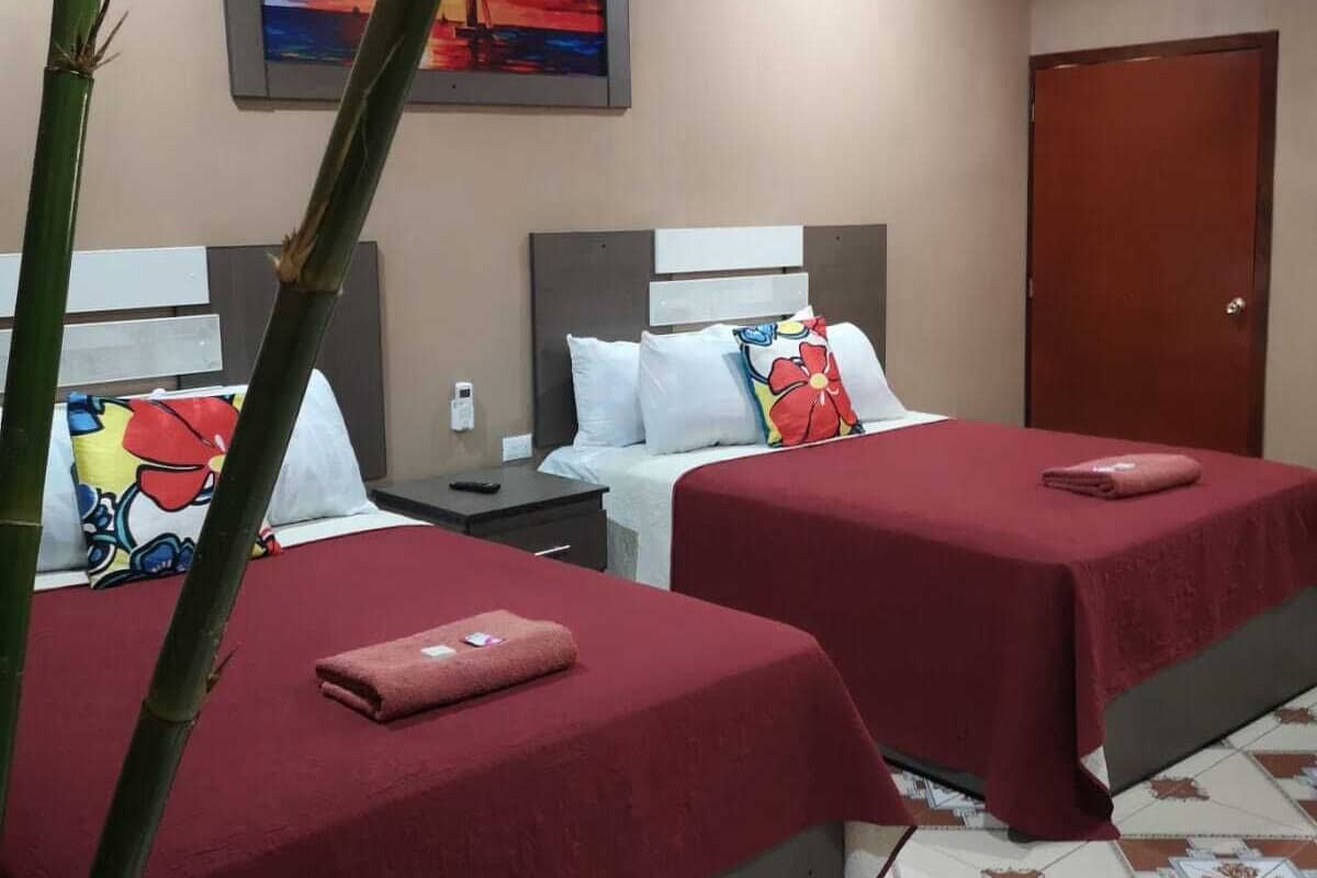 A hotel room with two beds, a painting on the wall, and a door.