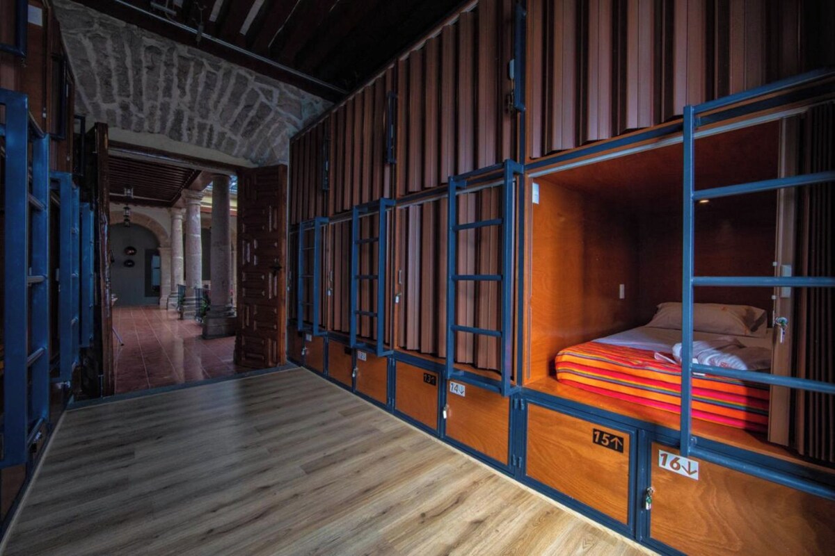 A room with a bed, a wooden floor, and a view of a stone wall.