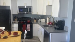 Une cuisine moderne avec des meubles blancs, un réfrigérateur noir, un four à micro-ondes, une cuisinière et un lave-vaisselle. On y trouve une table à manger recouverte d’une nappe jaune et agrémentée de bols rouges.