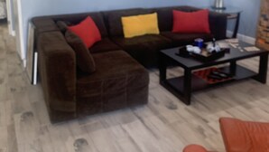 Un salon avec un canapé d’angle marron, une table basse et un fauteuil rouge. Il y a un tableau au mur et une lampe sur une table d’appoint.