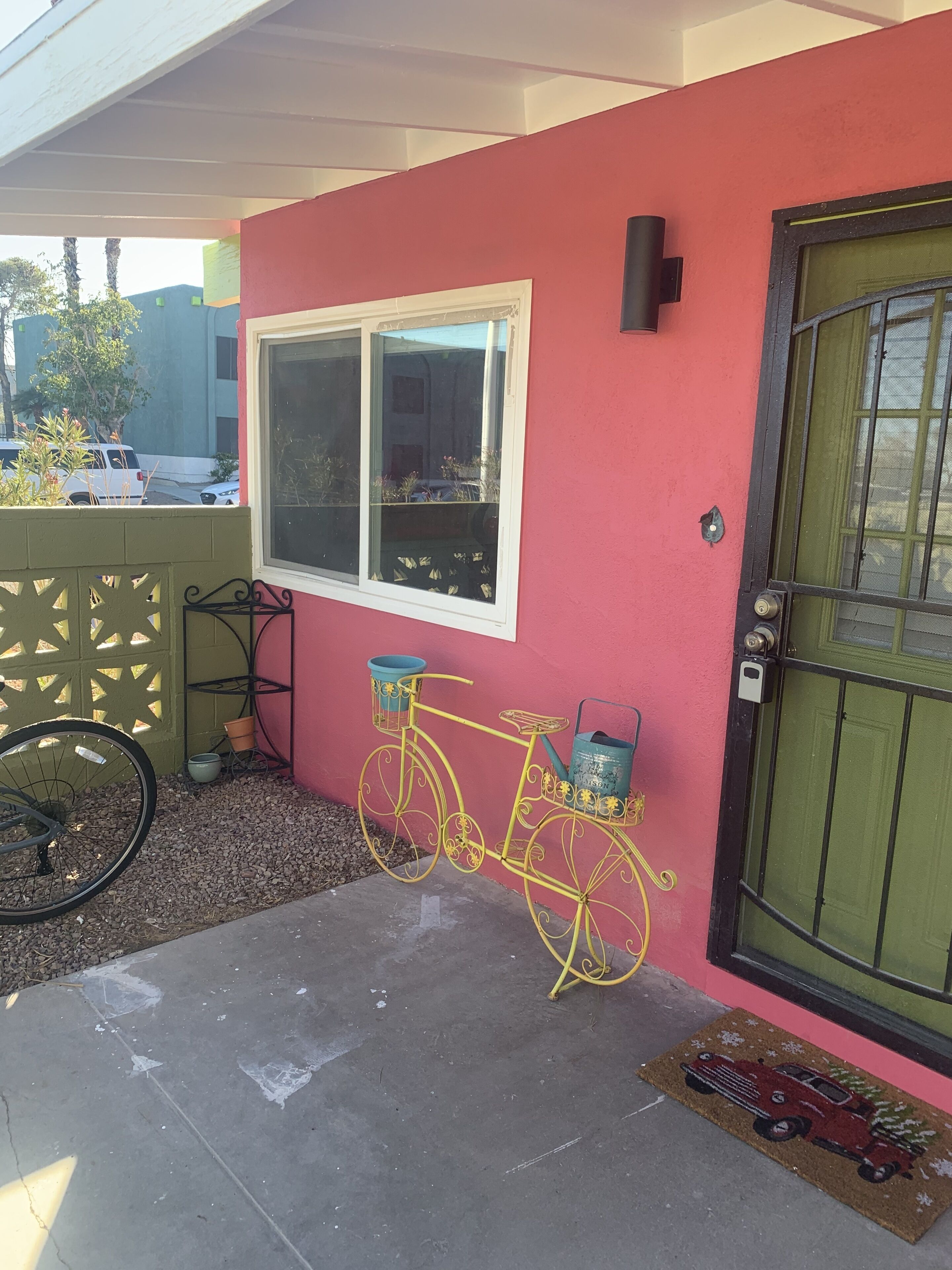 A red building with a yellow bicycle parked outside, a green door, and a window with a view of the street.