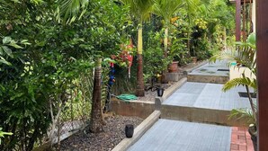 A pathway lined with palm trees and various plants, leading to a building with a wooden structure. - Milles Montagnes Residence (Mahé Island)