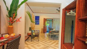 A room with a wooden floor, a dining table with chairs, a hanging plant, and a wooden cabinet with a hanger. - Milles Montagnes Residence (Mahé Island)