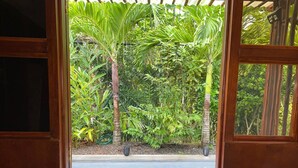 A wooden door with a "WELCOME" mat and a view of a garden with palm trees and other greenery. - Milles Montagnes Residence (Mahé Island)