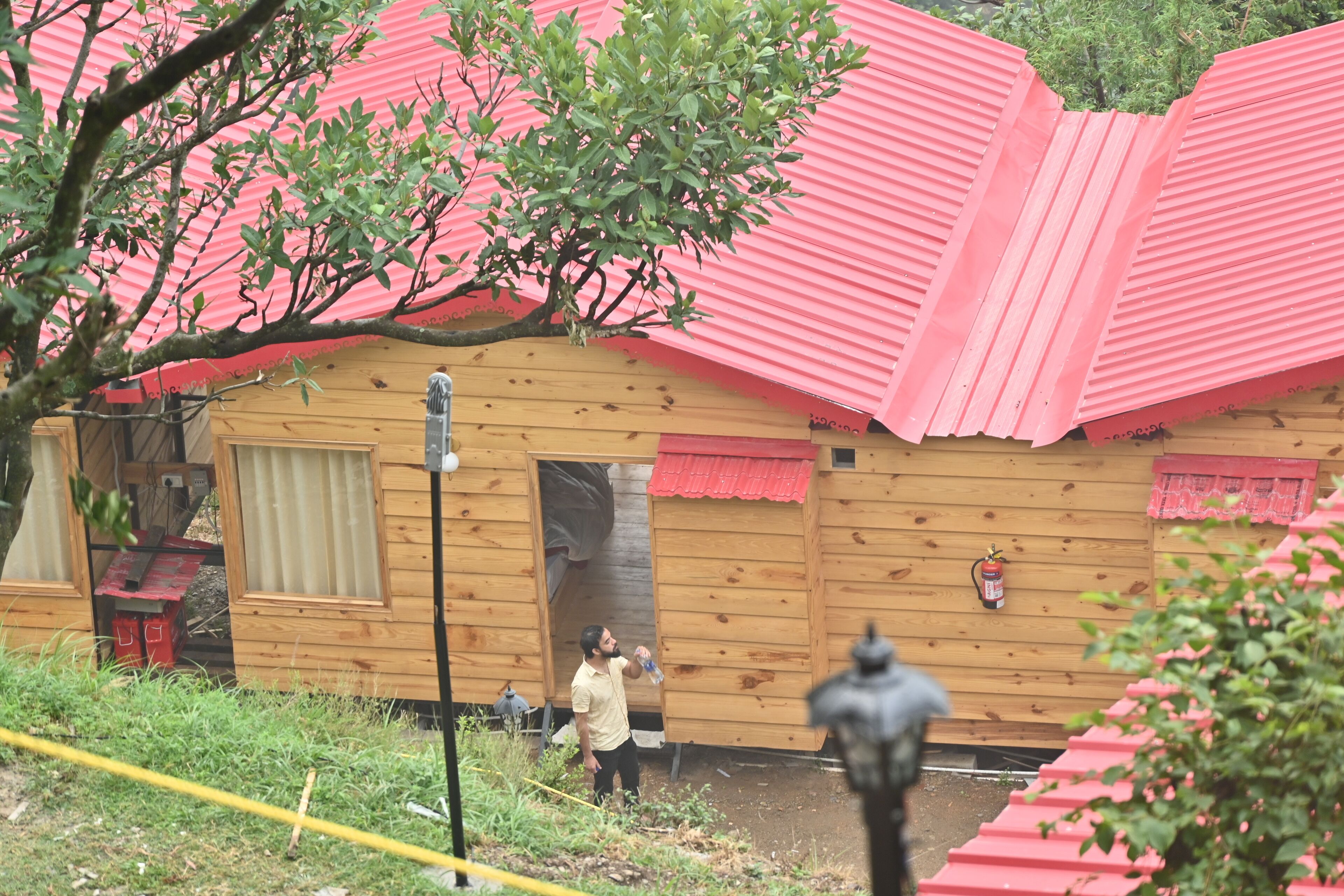 A wooden cabin with a red roof, a fire extinguisher mounted on the wall, and a small window.