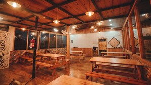Un interior rústico con mesas y bancos de madera, amplias ventanas y un muro de ladrillo.