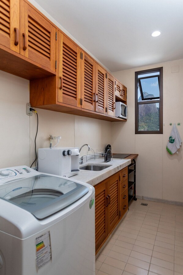 Una cocina compacta con armarios de madera, microondas integrado, lavadora y ventana con vistas.