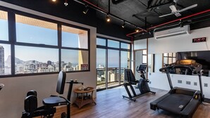 Ett gym med stora fönster, träningsutrustning och utsikt över staden.