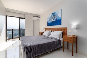 Une chambre moderne avec un grand lit, une table de chevet en bois, une lampe de chevet et une vue sur la ville par une grande fenêtre.