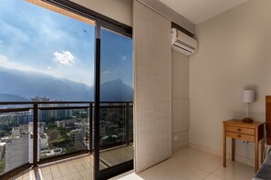 A modern bedroom with a large window, a wooden nightstand, and an air conditioning unit. - 1806 (Rio de Janeiro)