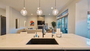 A modern kitchen with a large island, pendant lighting, and a view to the living area. - Spacious Home with Thunder Mountain Views! (Sedona)