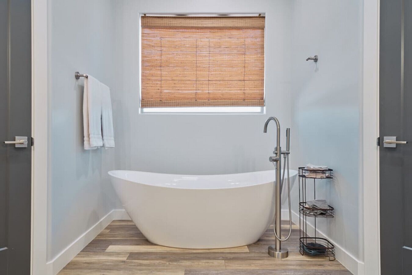 A modern bathroom with a freestanding bathtub, a window with blinds, and a towel rack.