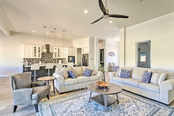 A modern living room with a sofa set, a coffee table, and a chair. There is a kitchen area in the background with white cabinets and a black and white backsplash.