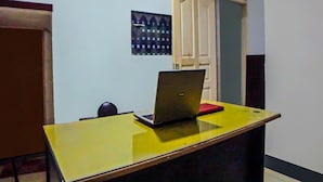 A room with a yellow desk, a laptop, and a red notebook. There is a door with a white frame and a wall with a patterned artwork. - Hotel O Guesthouse Rantang (Medan)