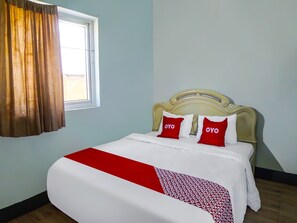 A neatly made bed with a white and red bedspread, two pillows with 'OYO' branding, a window with brown curtains, and a light blue wall. - Hotel O Guesthouse Rantang (Medan)