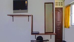 A room with a TV mounted on the wall, a wooden door, a window with yellow curtains, and a chair with a metal frame. - Hotel O Guesthouse Rantang (Medan)