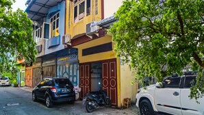 A street view with a building featuring a shop on the ground floor and a parked car and motorcycle on the sidewalk. - Hotel O Guesthouse Rantang (Medan)