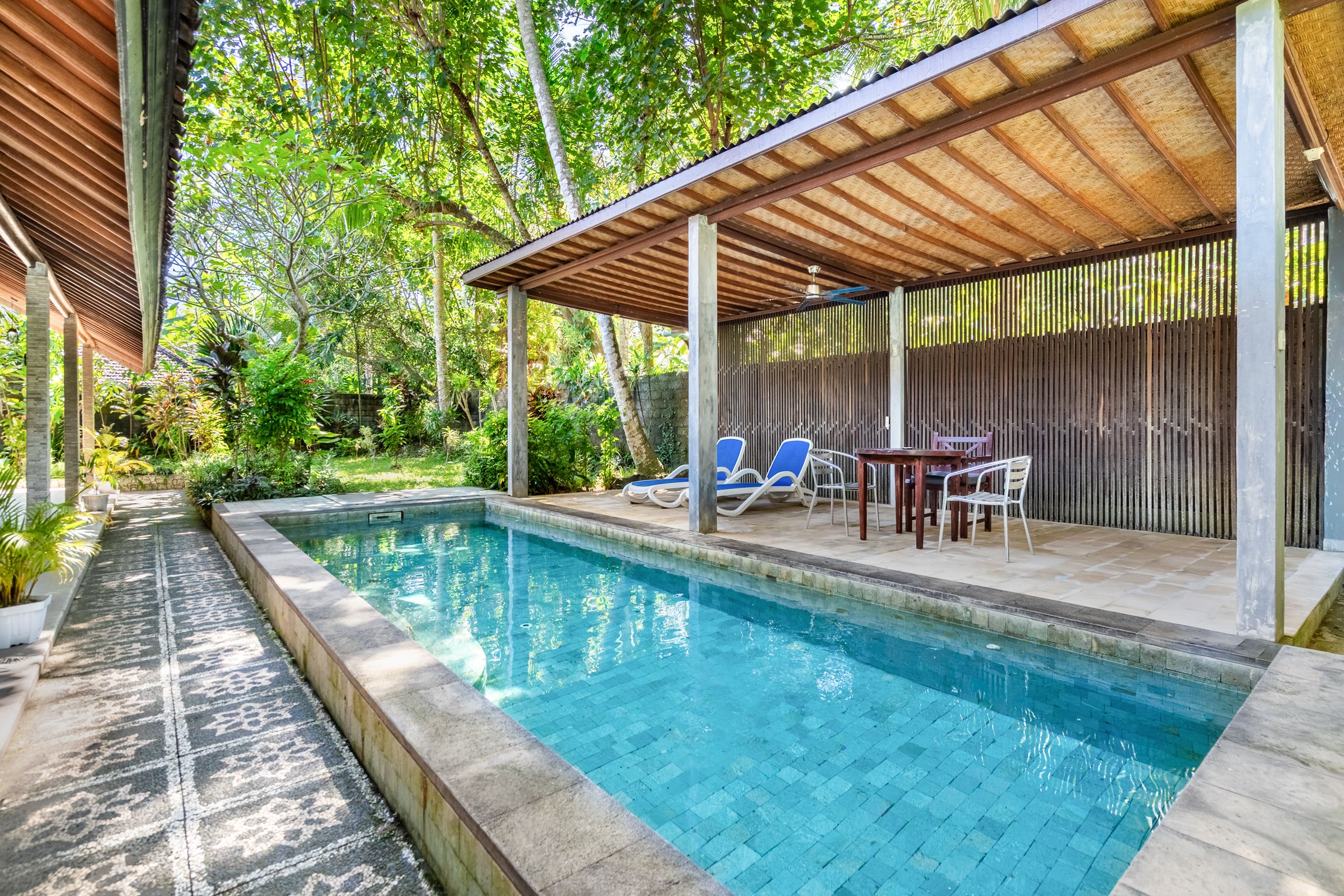 A swimming pool with a covered patio area, lounge chairs, and a table.