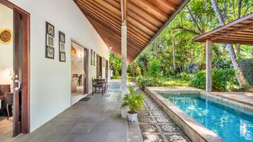 A covered outdoor area with a pool, a dining table with chairs, and a pathway leading to a door.