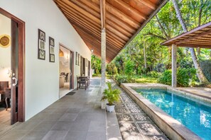 Un espacio exterior cubierto con una piscina, una mesa de comedor con sillas y un sendero que lleva a una puerta.