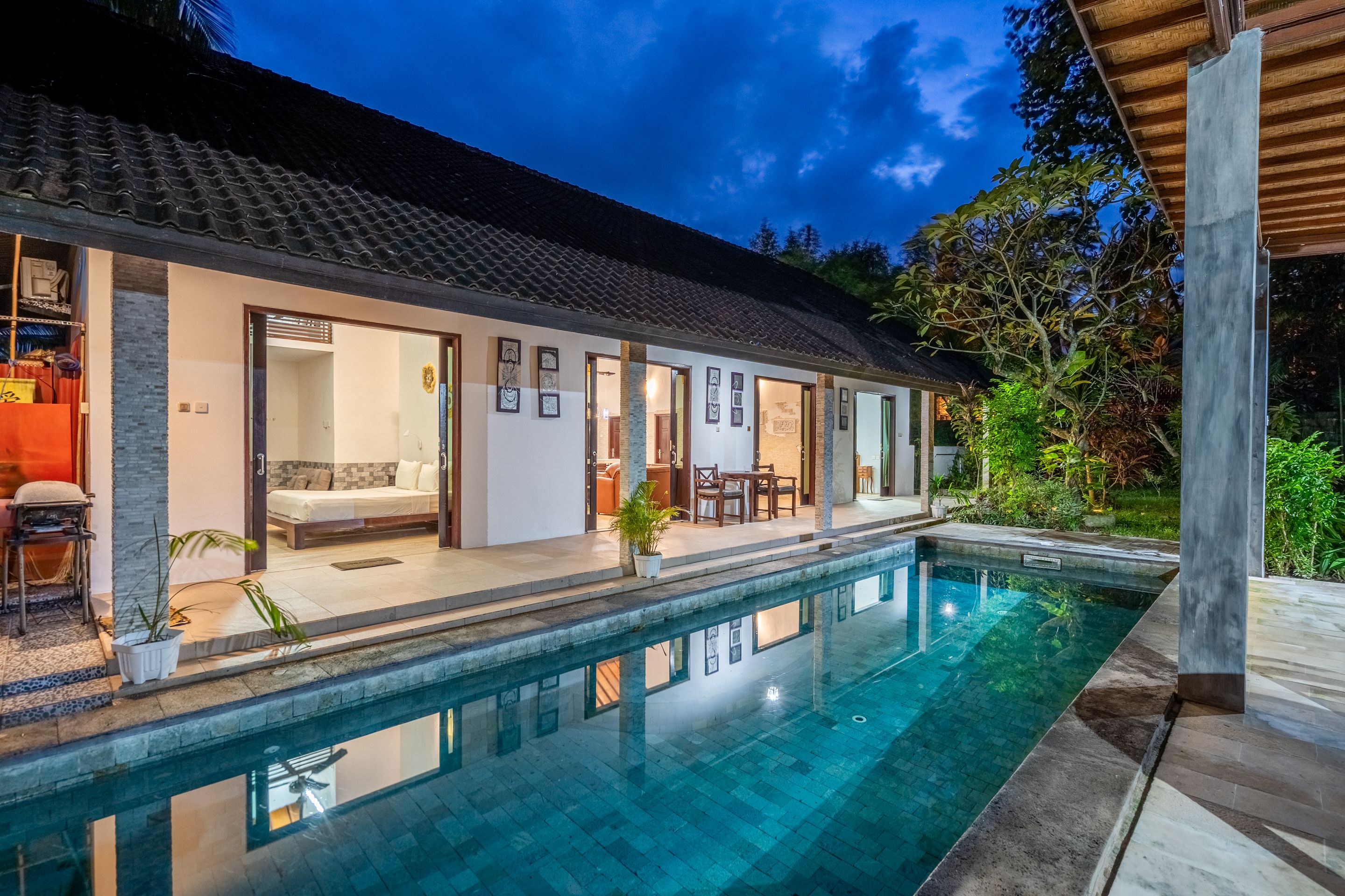 Una casa moderna con piscina, puertas abiertas que dan a un salón y un porche cubierto.