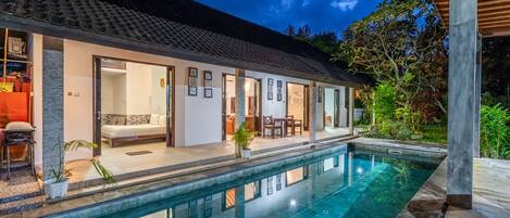 A modern house with a swimming pool, open doors leading to a living area, and a covered patio.