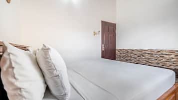 Ein Zimmer mit einem Bett, einem Holzkopfende, einer Tür und einer Wand mit strukturierter Oberfläche.
