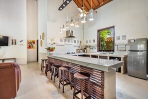 A modern kitchen with a central island, bar stools, a stainless steel refrigerator, and pendant lighting.