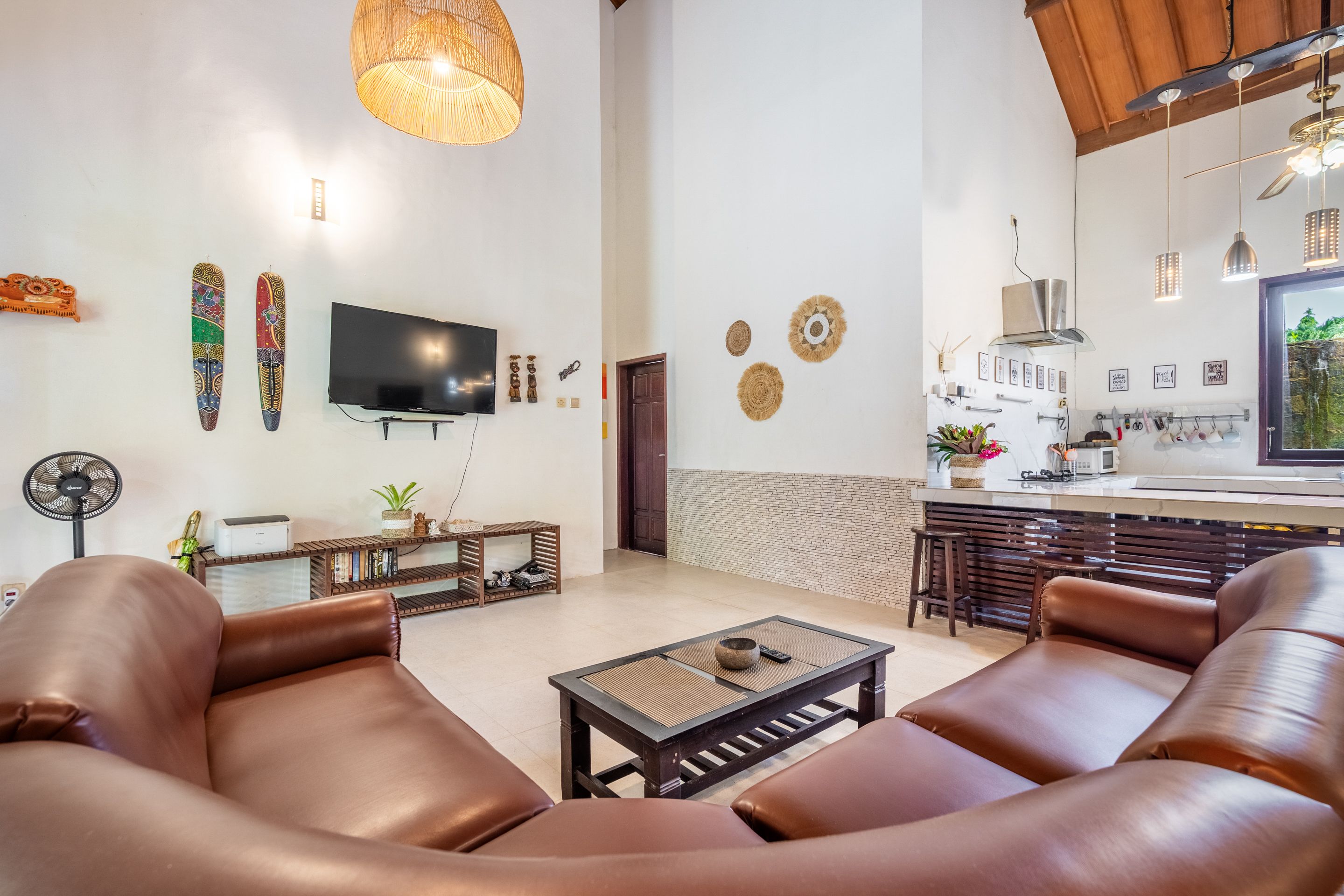 A modern living room with leather sofas, a flat-screen TV, and a dining area with a kitchen in the background.