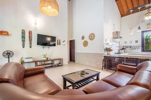 A modern living room with leather sofas, a flat-screen TV, and a dining area with a kitchen in the background.