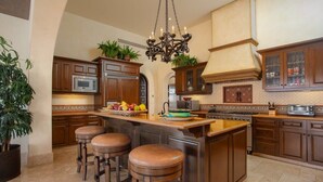 A spacious kitchen with wooden cabinets, a central island with stools, a chandelier, and potted plants. - Fundadores 121 - Puerto Los Cabos (San Jose Del Cabo)