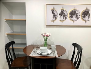 A dining area with a round table, two chairs, a vase with flowers, and a framed artwork above the table.