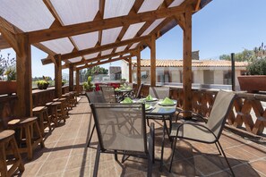 An outdoor patio with wooden tables and chairs, a covered seating area, and a view of buildings in the background. - Collection O Cachito Mio (San Pedro Cholula)