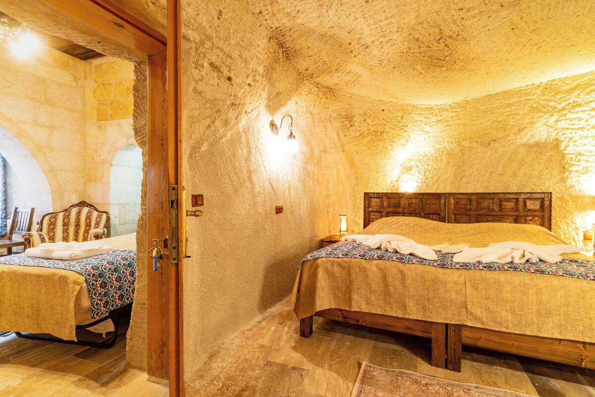 A cozy bedroom with a stone wall, a wooden bed, and a nightstand with a lamp.