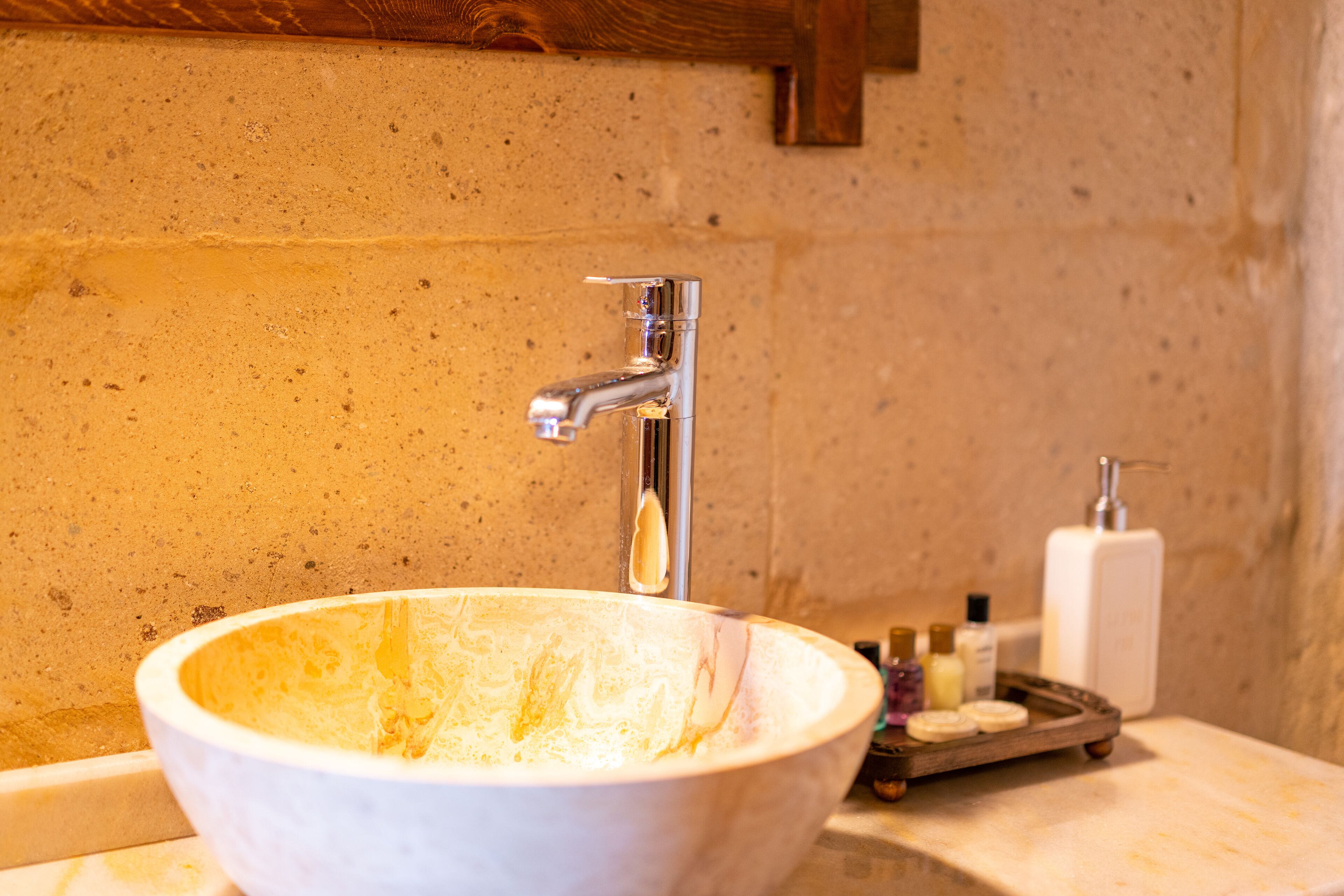 A bathroom with a large white sink, a chrome faucet, and a wooden tray with toiletries.