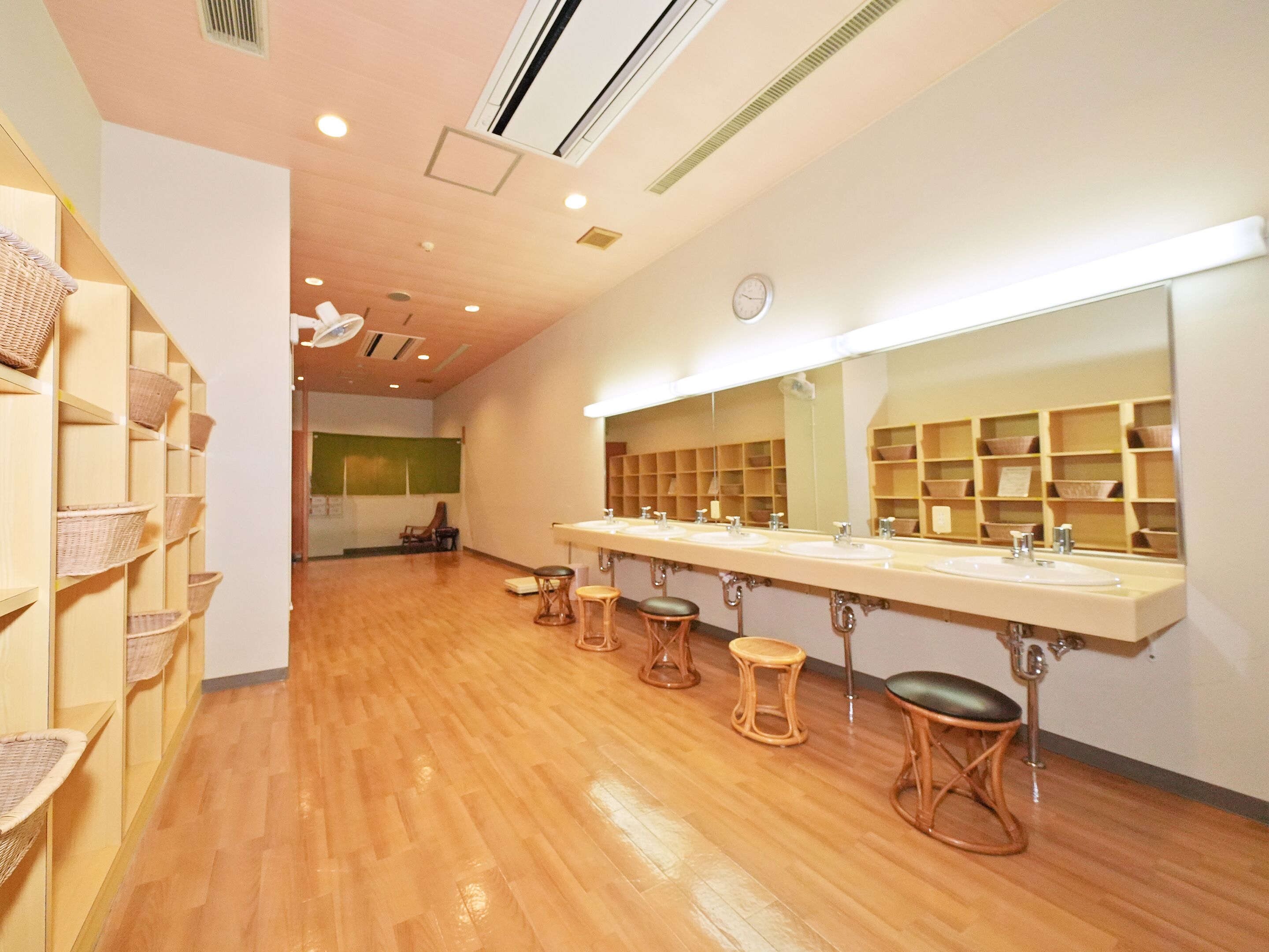 A bathroom with wooden floors, a large mirror, and shelves with baskets.