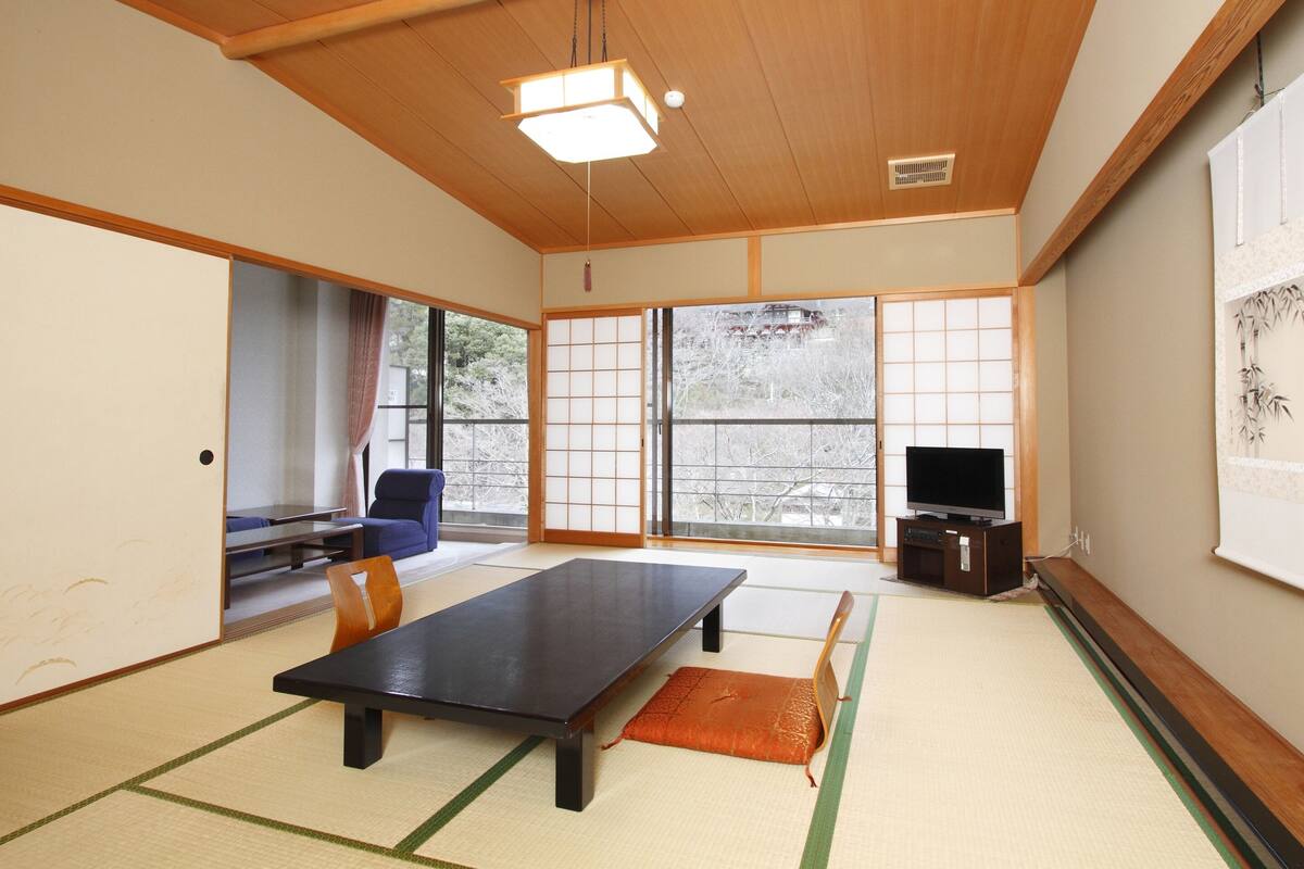 A traditional Japanese room with tatami flooring, a low table, a blue chair, and a television.