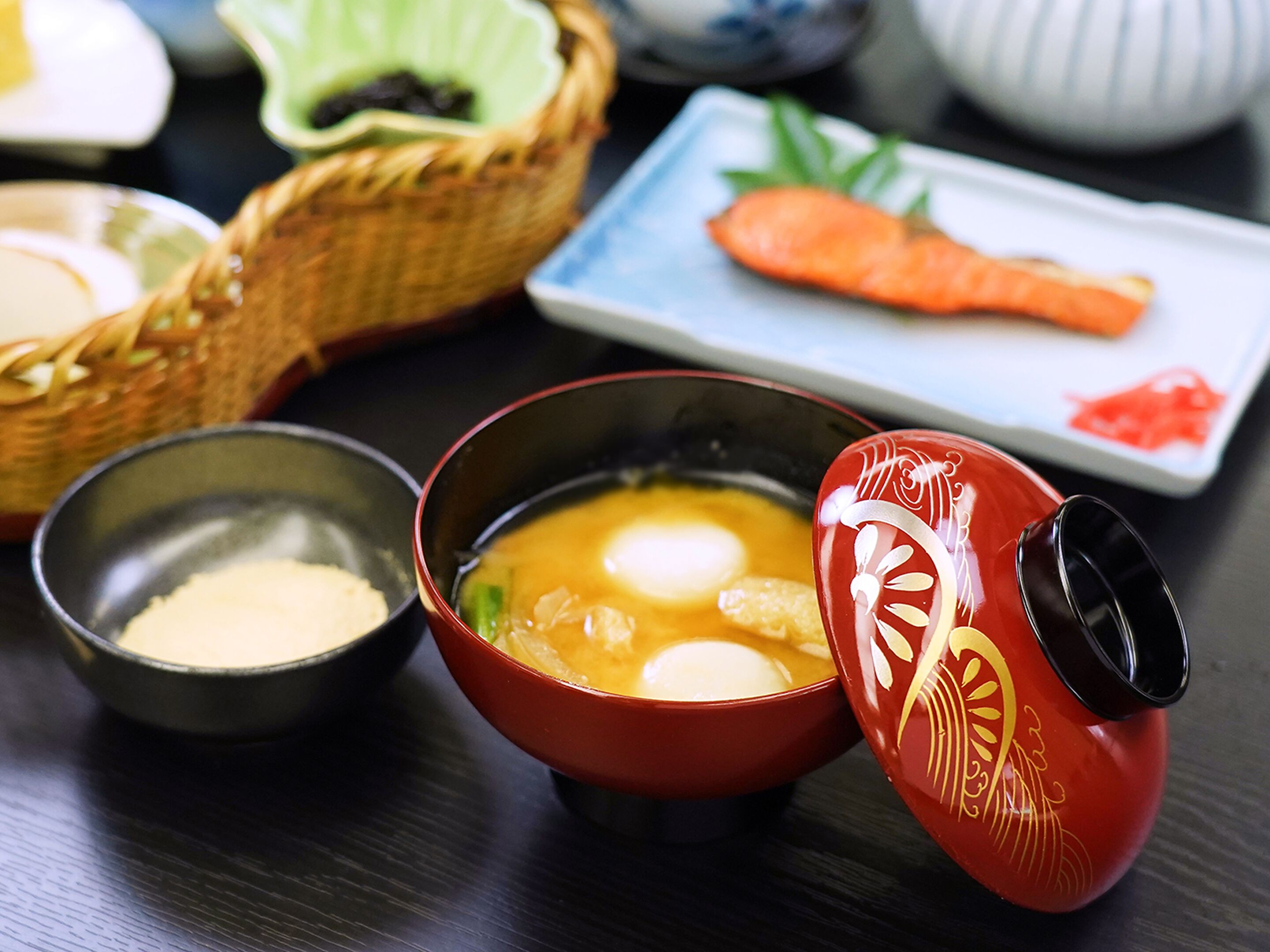 A traditional Japanese meal setup with a bowl of soup, a small bowl of miso, a ceramic pitcher, and a plate with a salmon sashimi.