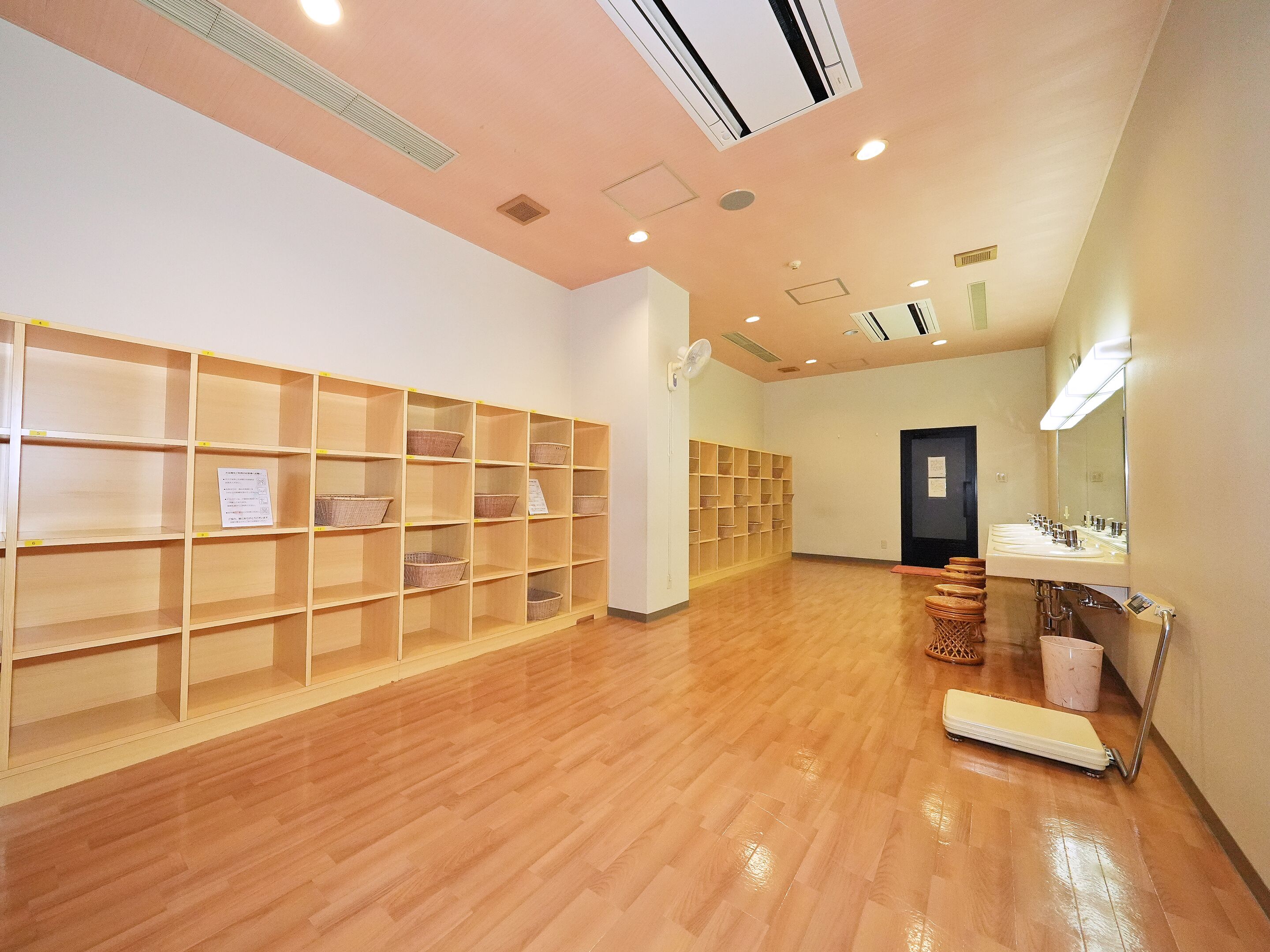 A hotel lobby with wooden shelving units, a reception desk, and a bathroom with a sink and mirror.