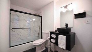 A modern bathroom with a glass-enclosed shower, a white toilet, a black sink with a mirror above it, and a towel rack with towels.