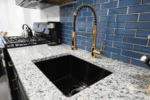 Una cocina con encimera de granito, pileta de acero inoxidable, grifo dorado y salpicadero con azulejos azules.