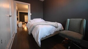Quarto com cama, uma cadeira e porta que dá para outro cômodo.
