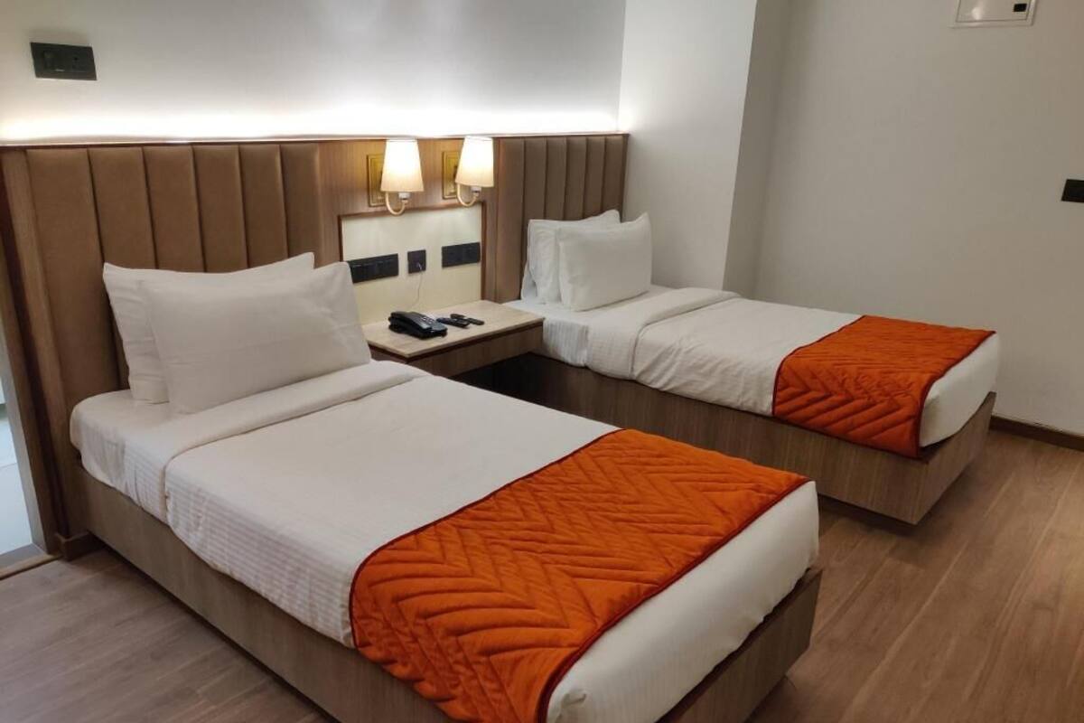 A hotel room with two beds, each with a headboard, a bedside table with a lamp, and a telephone.