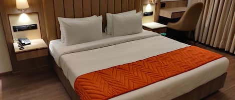 Una habitación de hotel con una cama grande, dos mesitas de noche con lámparas, una silla y una ventana con cortinas.