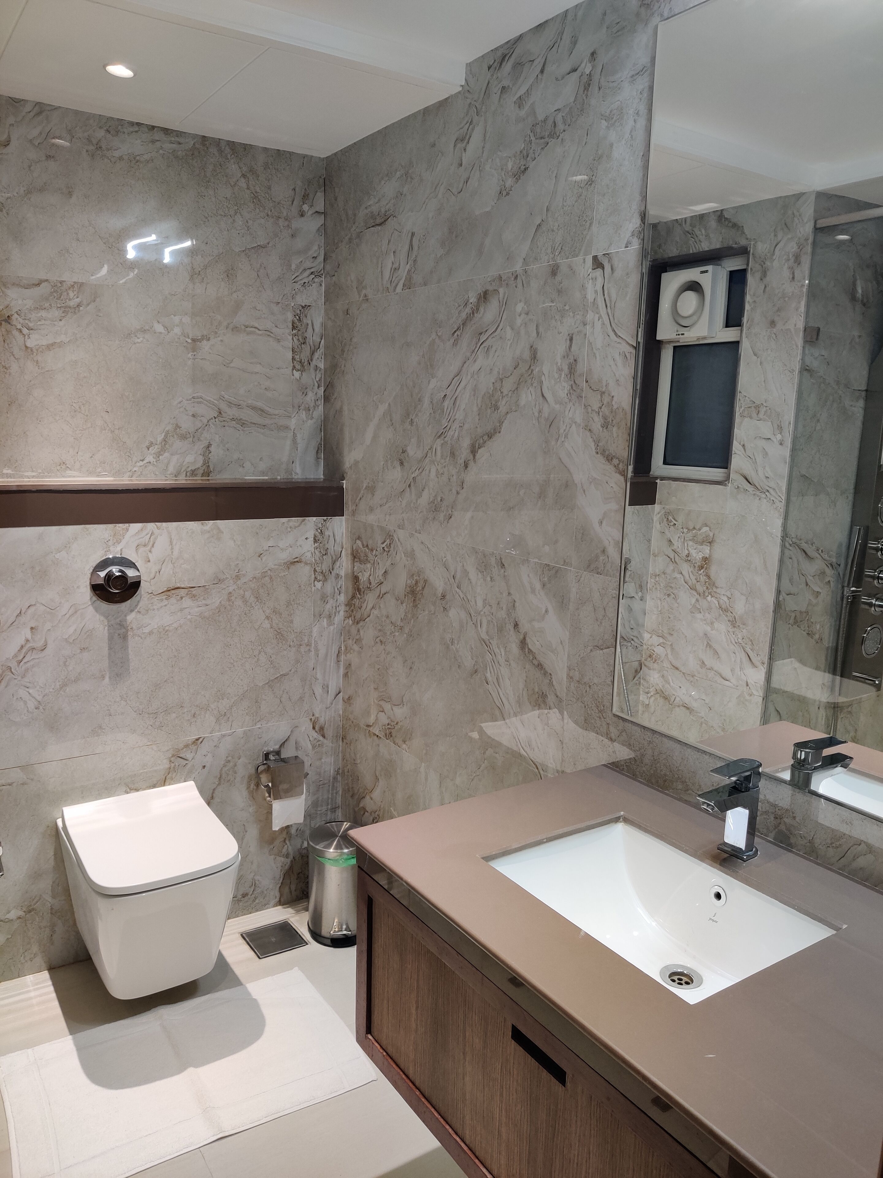 Un baño moderno con pared de mármol, inodoro, lavamanos y espejo.