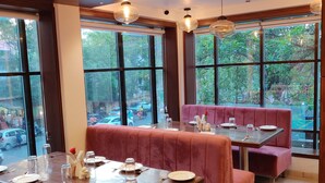 Un restaurante con asientos tapizados en rojo y mesas, ventanas amplias con vista a la calle e iluminación colgante.